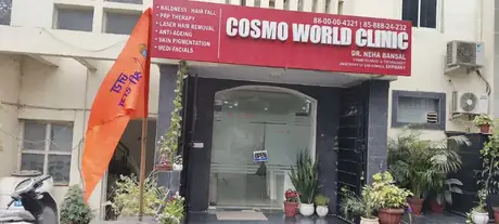 A wider street-level view of the same red signboard and glass entrance, with an orange flag on a pole at the left, an OPEN sign hanging on the door and rows of potted plants across the front.